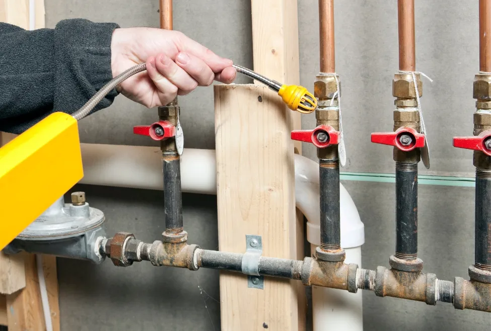 Licensed plumber using an electronic gas leak detector on indoor gas line valves to ensure safety and code compliance