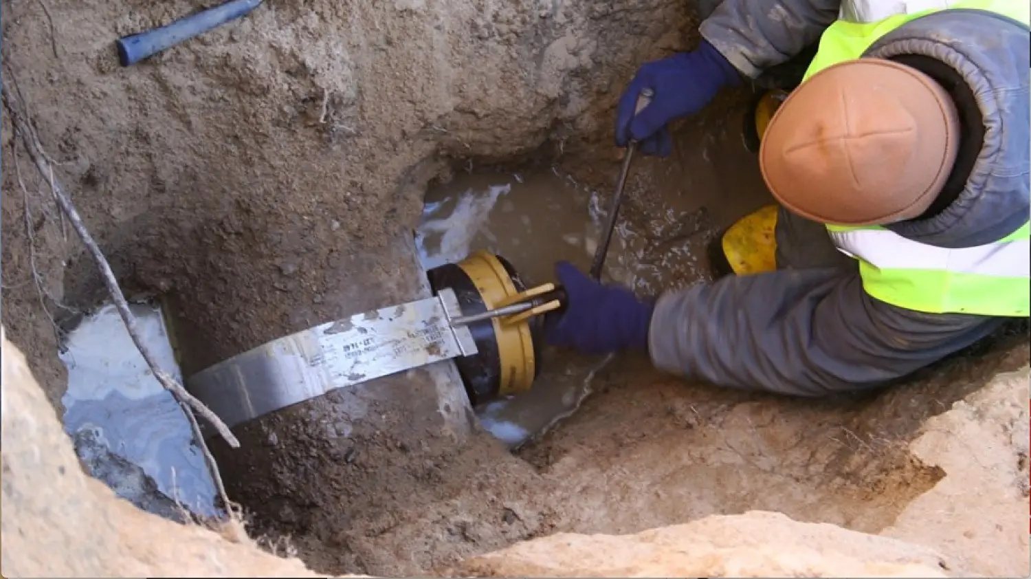 Licensed plumber performing a traditional sewer line repair by installing a structural clamp on a pipe in an excavated trench