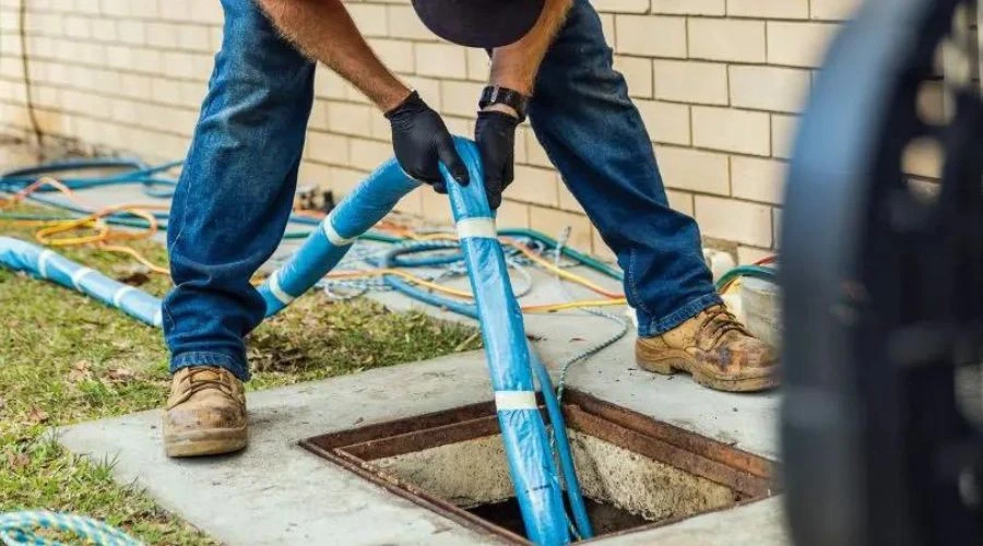 Professional plumber installing a blue epoxy-saturated pipe liner into a sewer access point for a trenchless repair project